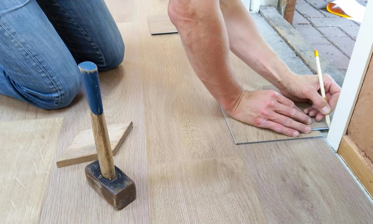 A homeowner drawing a line with a pencil while installing light wood floors