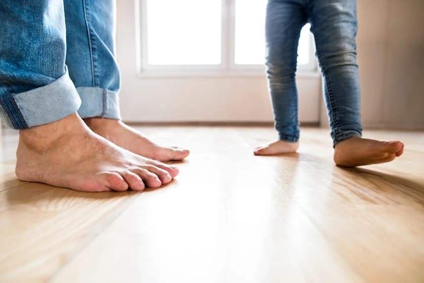 two pairs of feet close up on a wood floor - one of a father, the other of a child